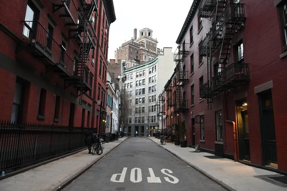 The photo captures a quiet urban street flanked by red brick buildings with fire escapes leading up to a taller building at the end with the word STOP painted in reverse on the pavement indicating the view is from the wrong way down a one-way street