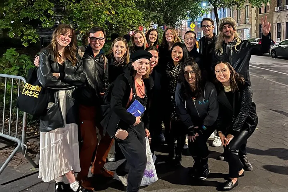 A group of smiling people pose for a nighttime photo on a city street