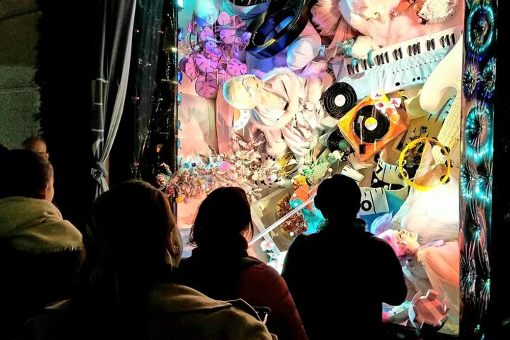Spectators are viewing a vibrantly illuminated colorful window display with an elaborate and artistic arrangement