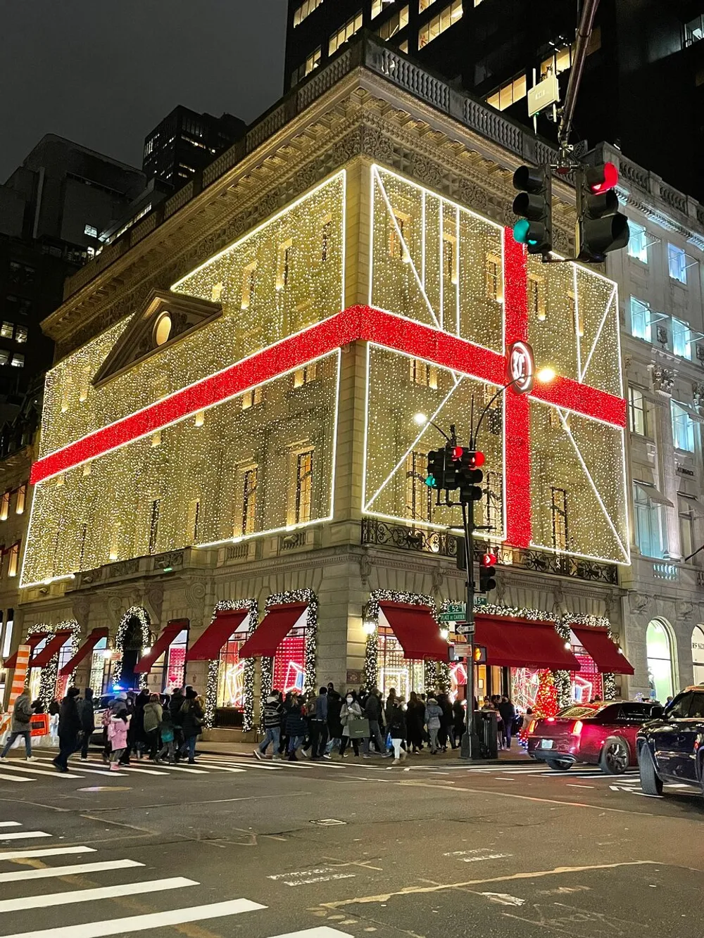 A building is extravagantly adorned with holiday lighting and decorations as pedestrians walk by on the street corner at night