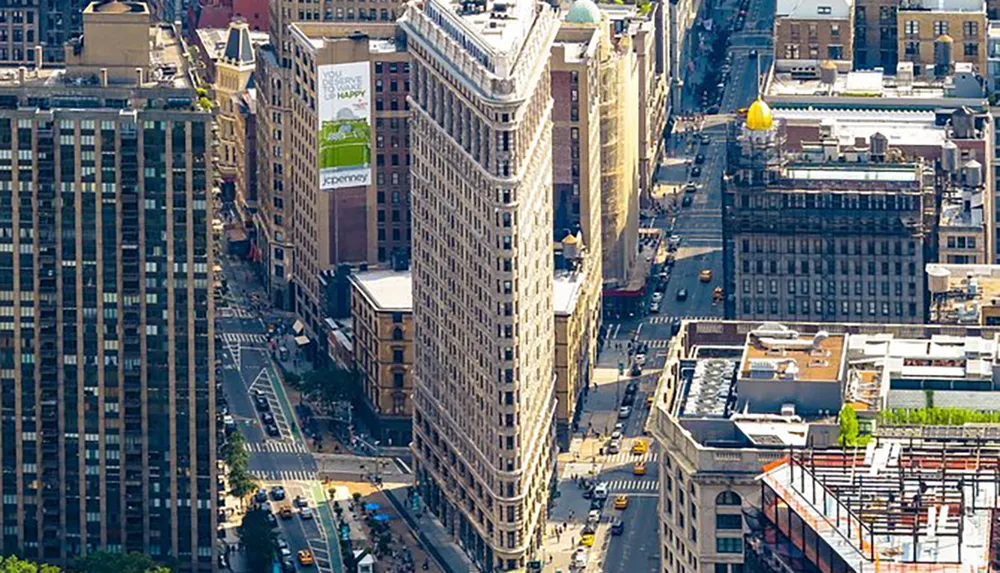 The image shows an aerial view of the Flatiron Building a distinctive triangular skyscraper in Manhattan New York City amidst its urban surroundings on a sunny day