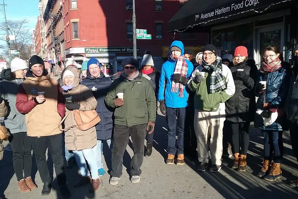 A group of people are standing on a sunny winter day many holding cups and appearing to be in good spirits