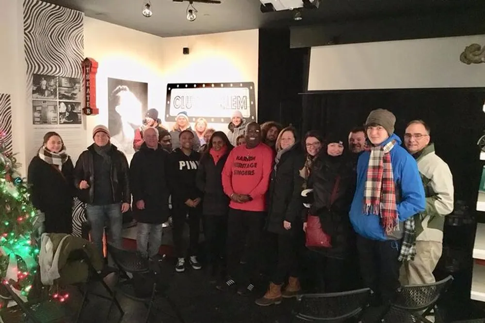 A group of people are posing for a photo in a cozy room with cinema-themed decor including a Christmas tree on the left and a movie screen in the background