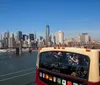 Tourists enjoy a guided bus tour with a view of the Manhattan skyline and Brooklyn Bridge under a clear blue sky