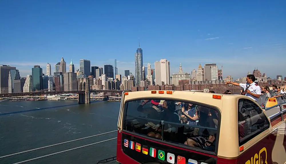 Tourists enjoy a guided bus tour with a view of the Manhattan skyline and Brooklyn Bridge under a clear blue sky