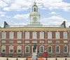 The image shows Independence Hall with a clock tower in Philadelphia a historical building against a blue sky with a statue standing prominently in its courtyard