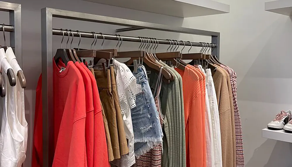 The image shows a variety of womens clothing items neatly displayed on hangers in a retail store setting with a mirror in the background indicating a fitting area