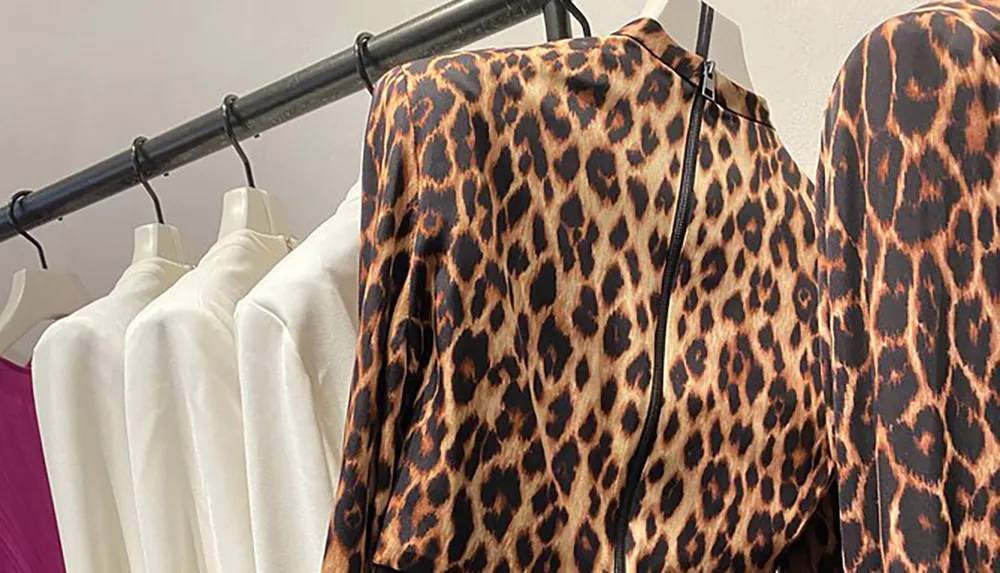 A clothing rack displays various apparel including a leopard print top among predominantly white garments