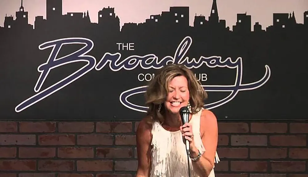 A person is performing stand-up comedy at The Broadway Comedy Club as indicated by the backdrop