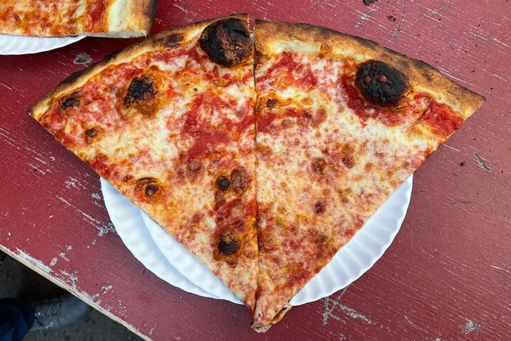Two large slices of cheese pizza rest on a paper plate atop a red wooden table