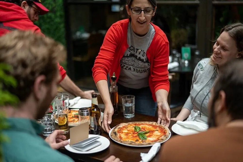 A woman in a red shirt is serving pizza to a table of people at a casual dining establishment