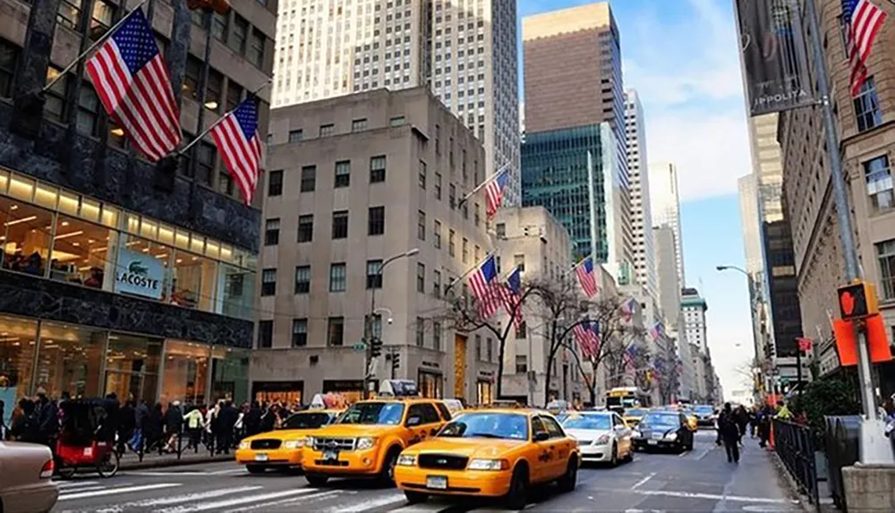 Yellow taxis navigate a bustling street lined with American flags in a cityscape likely to be New York