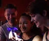 Three smiling people are looking at a glowing blue diamond-shaped object that one person is holding in their hand