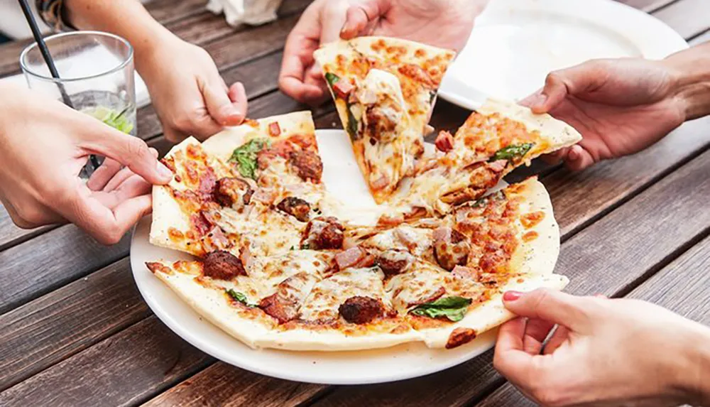 Several people are sharing a large pizza with toppings at a wooden table