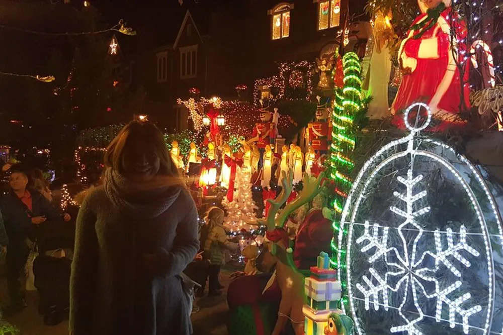 A person is standing in front of a vibrant and intricately decorated house with festive lights and Christmas decorations