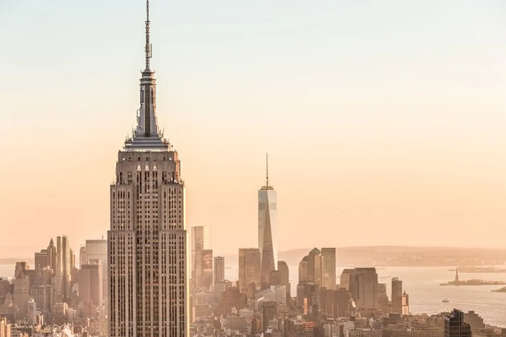 The image features the Empire State Building in the foreground with the skyline of Lower Manhattan in the background bathed in the warm glow of a sunset