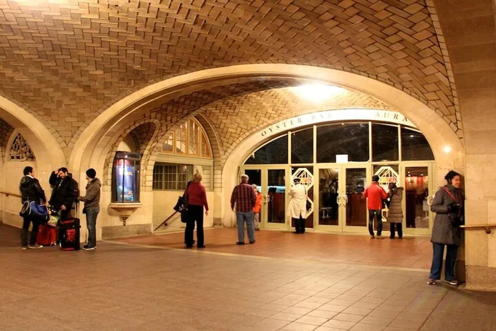 Travelers and visitors are standing outside an arched entrance of a grand building with the inscription Oyster Bar  Restaurant