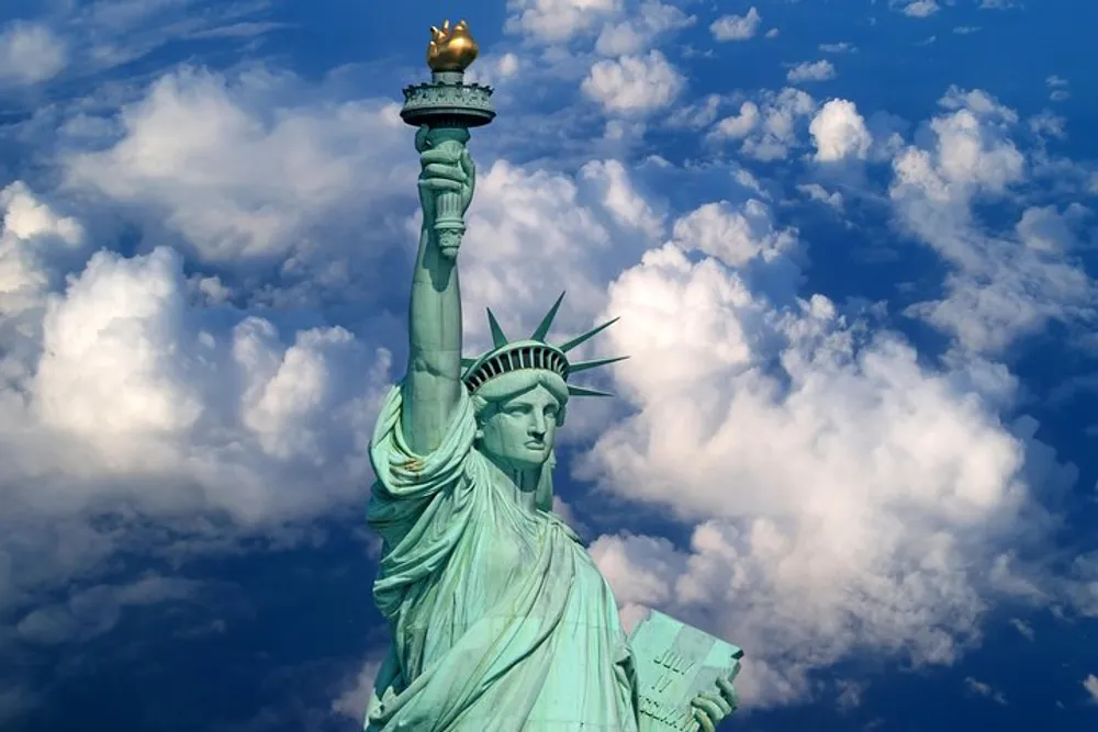 The Statue of Liberty is depicted against a backdrop of a blue sky with fluffy white clouds