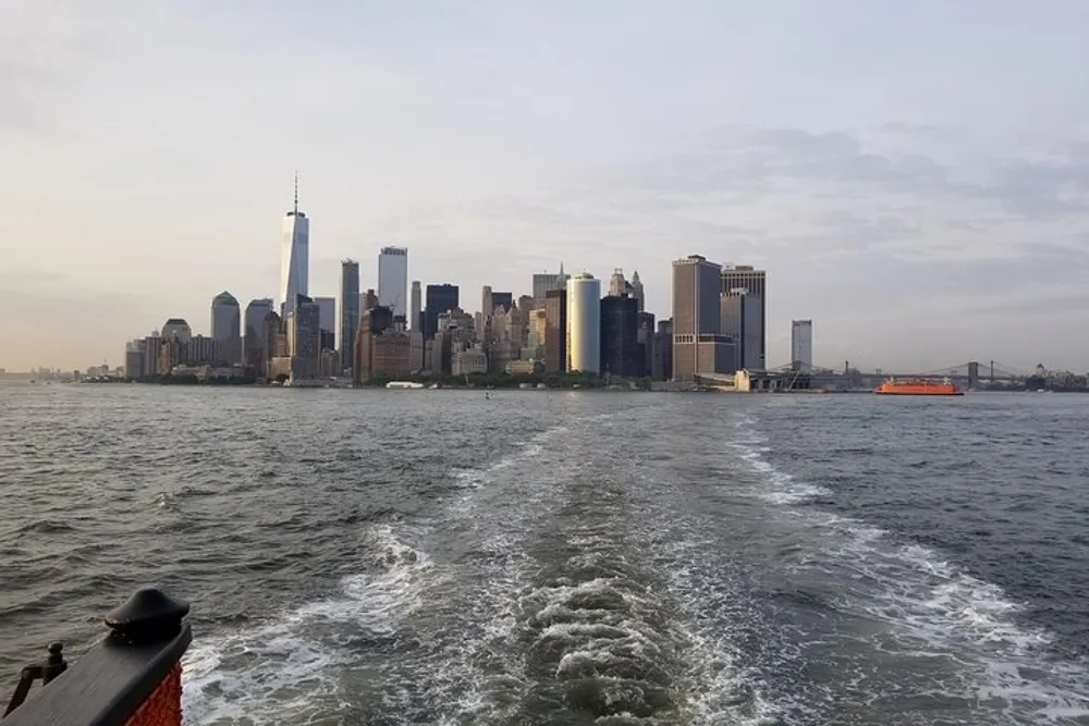 A view from a boat showing the wake on the water with the Lower Manhattan skyline in the background during early evening light