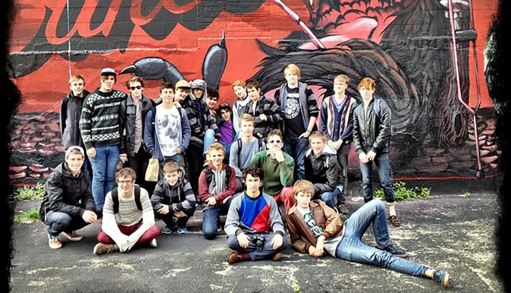 A group of young people poses for a photograph in front of a wall with a large colorful graffiti mural
