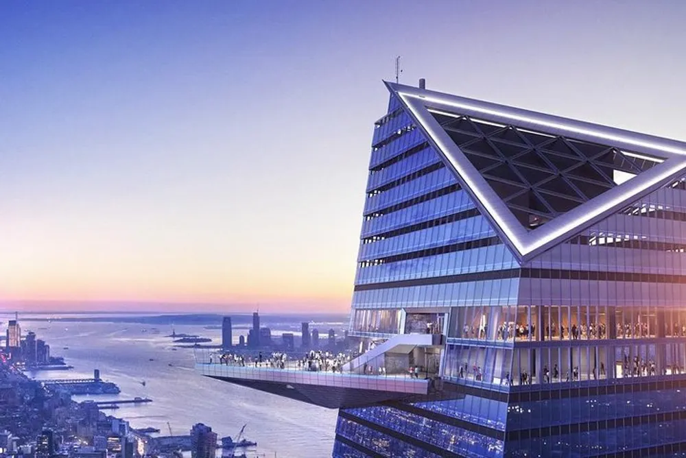 The image shows a modern skyscraper with a distinctive triangular upper structure featuring an observation deck with visitors enjoying the view at dusk overlooking a city skyline and river