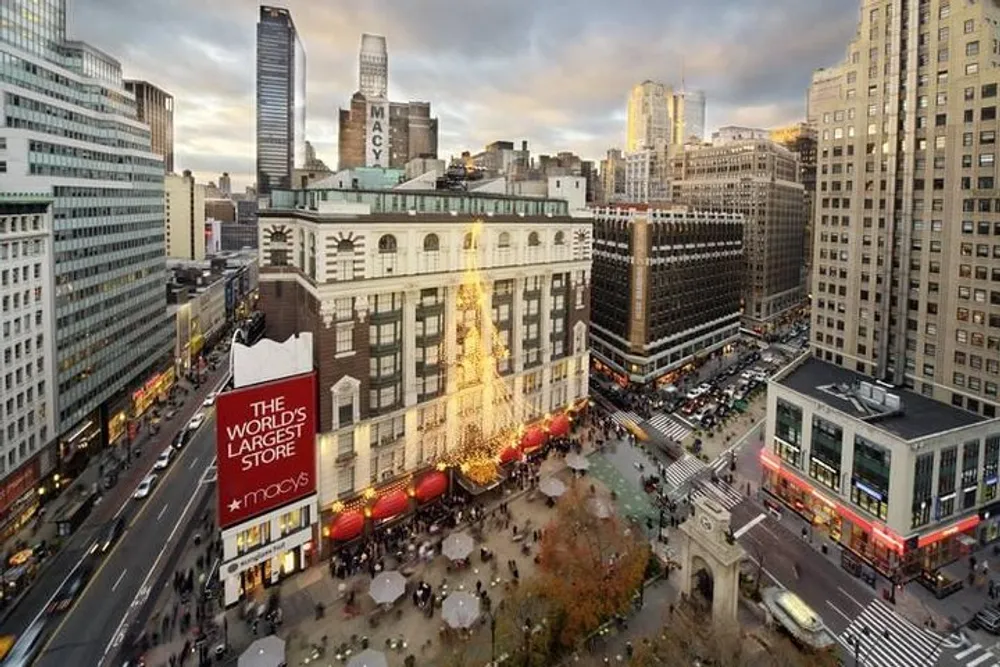 The image shows an aerial view of Macys department store at the corner of a bustling city intersection with holiday decorations and a crowd of people set against a backdrop of skyscrapers under a cloudy sky