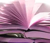 The image shows an open book with its pages fanned out revealing purple-tinted edges and casting a soft shadow on a light background