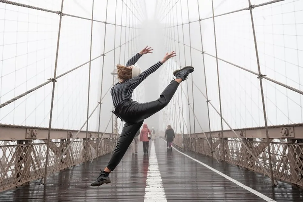 A person is performing a high kick on a foggy bridge with pedestrians in the background