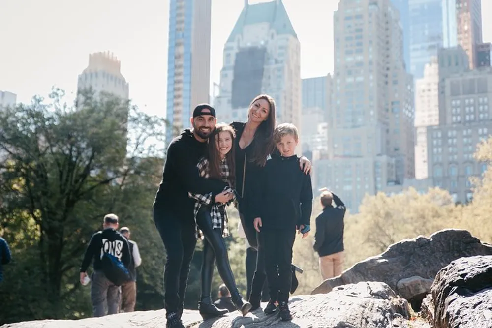 A group of people is posing for a photo on a rocky outcrop with the backdrop of tall city buildings on a sunny day
