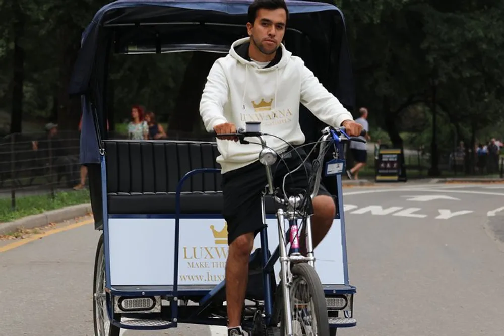 A man is pedaling a pedal-powered rickshaw on a park road appearing focused on his path ahead