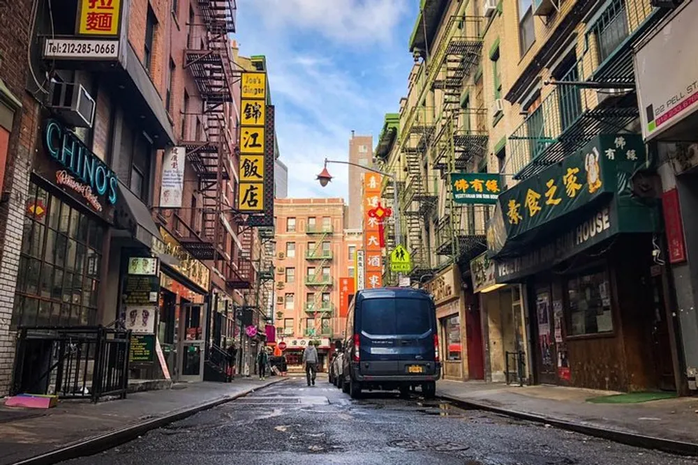 A quiet street scene likely in a citys Chinatown showing various signs in Chinese a parked van and a few pedestrians walking on the sidewalk