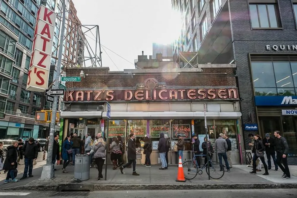 A group of people is gathered outside Katzs Delicatessen a famous eatery with a vintage facade on a busy city street