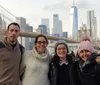 Four people are posing for a photo with the Brooklyn Bridge and the New York City skyline including the One World Trade Center in the background