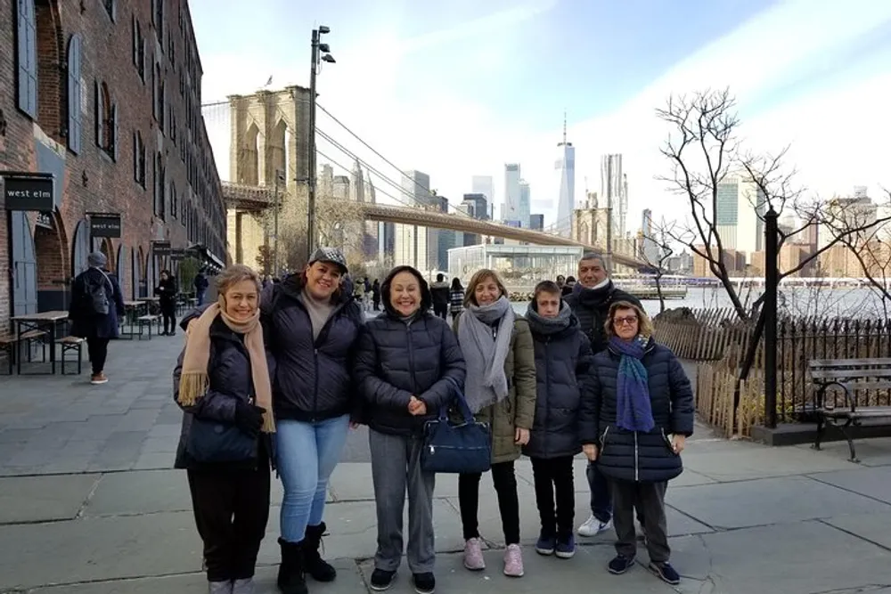 A group of happy people posed for a photo on a clear day with the Brooklyn Bridge and Manhattan skyline in the background