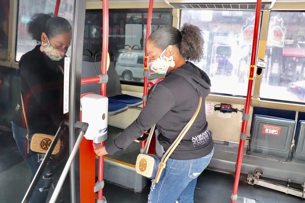 A person is using a hand sanitizer dispenser on a public bus while wearing a face mask