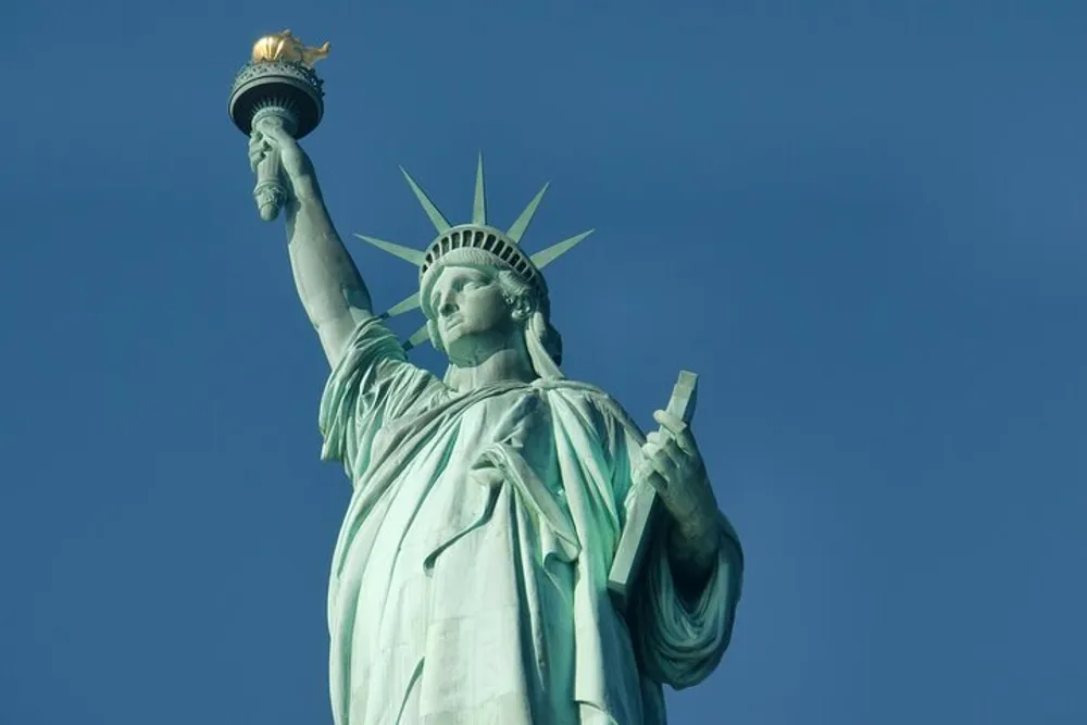 The image shows the Statue of Liberty against a clear blue sky detailed with its iconic raised torch and crown