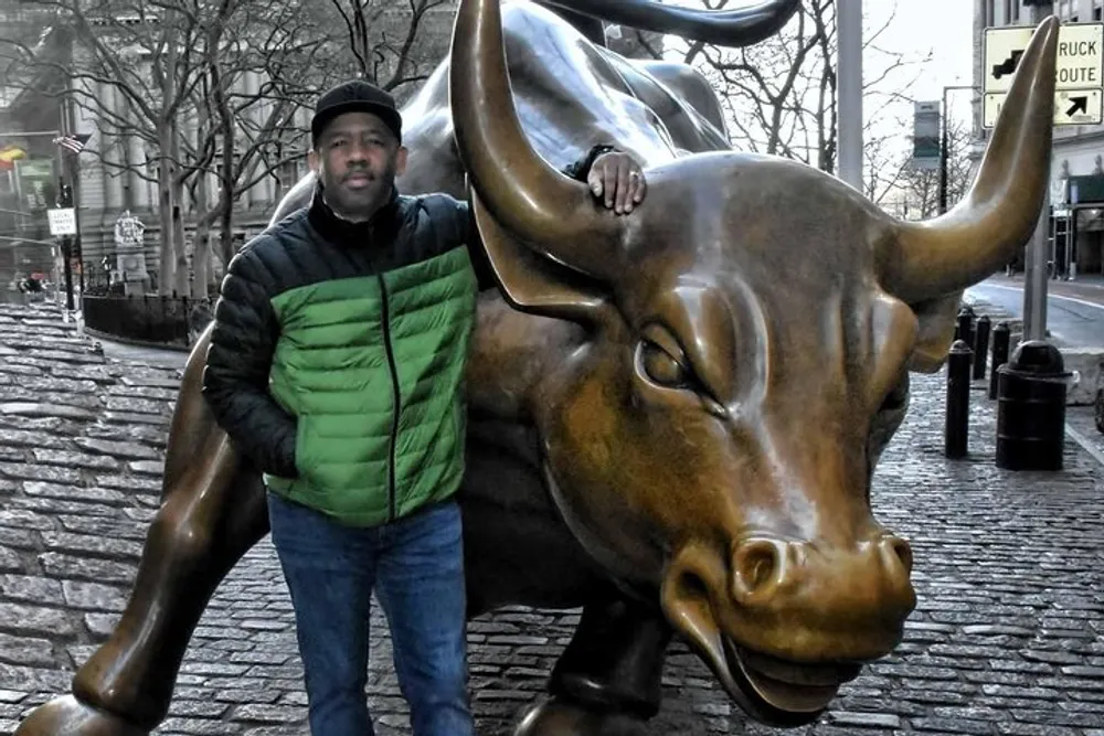 A person is posing with the Charging Bull statue which is a symbol of financial optimism and prosperity located in the Financial District of Manhattan New York City