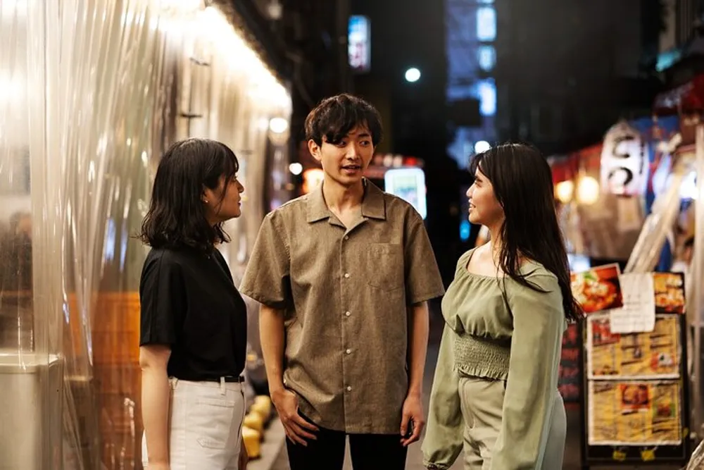 Three people are engaging in a conversation on a lively street adorned with lights and restaurant signs at night