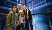 A family of four appears fascinated by something they are observing inside a glass elevator.