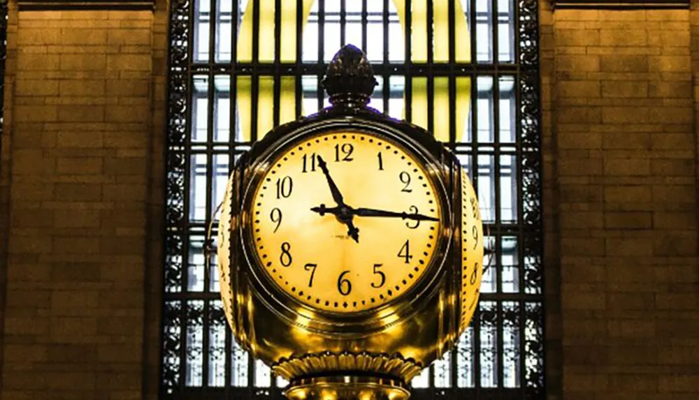 The image features a large golden clock hanging inside a building with a tall window in the background