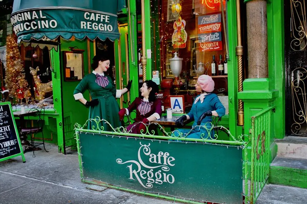 Three individuals are seated and interacting in front of a vibrant green caf named Caff Reggio adorned with festive decorations and the sign Original Cappuccino