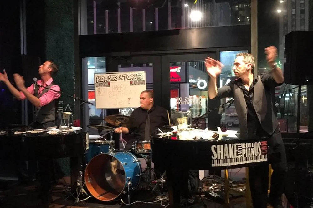 A three-person band is performing at a venue with a keyboardist and a standing singer in the foreground and a drummer in the background