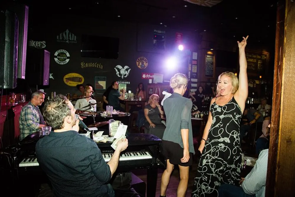 A lively scene at a bar with a woman raising her arm in excitement near a pianist while patrons enjoy the atmosphere