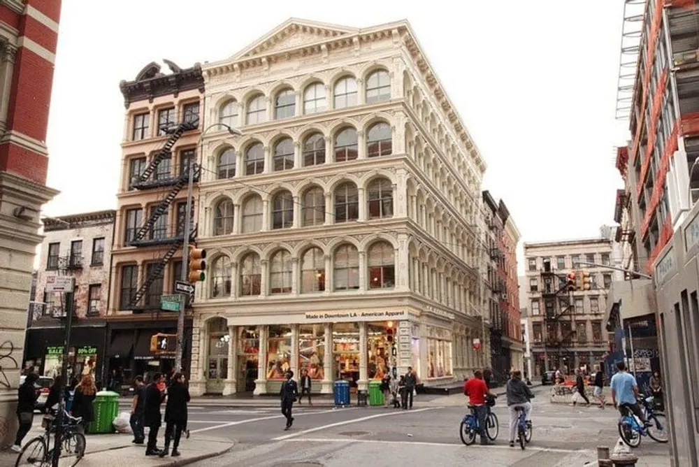 The image shows a bustling street corner in an urban environment with pedestrians and cyclists featuring a prominent classic multi-story building housing a retail store