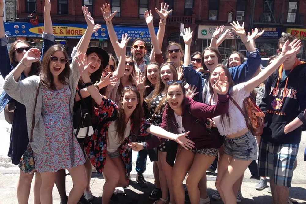 A group of cheerful people are posing for the camera with raised arms and wide smiles on a sunny day in an urban setting