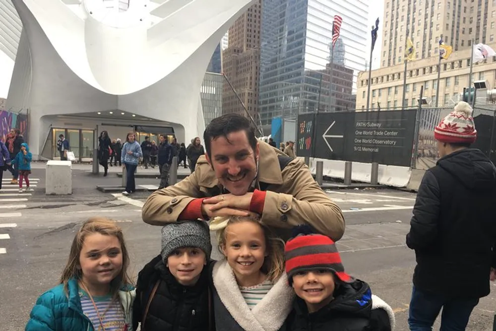 A smiling man is posing with four happy children in front of the Oculus structure at the World Trade Center in New York City