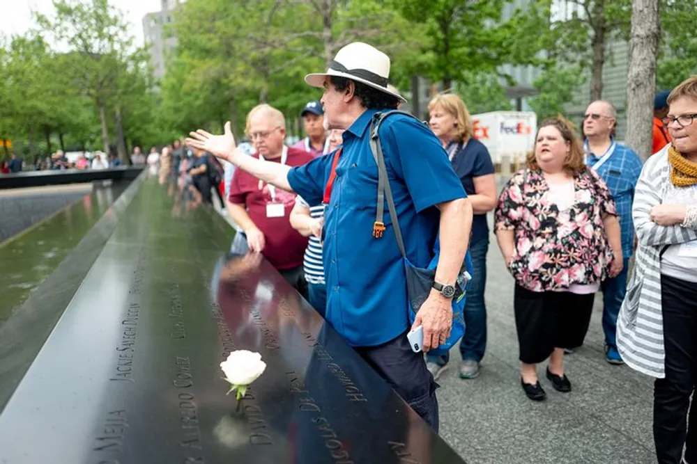 Visitors are paying their respects at a memorial with names engraved on its surface with one person reaching out to touch the names while others look on