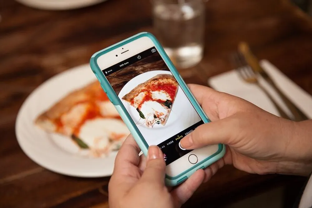 A person is taking a close-up photo of a slice of pizza on a plate using a smartphone