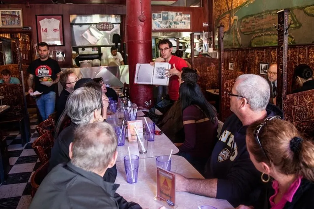A group of people is sitting at a restaurant table being attended to by a server while other patrons and staff carry on with their activities in the background
