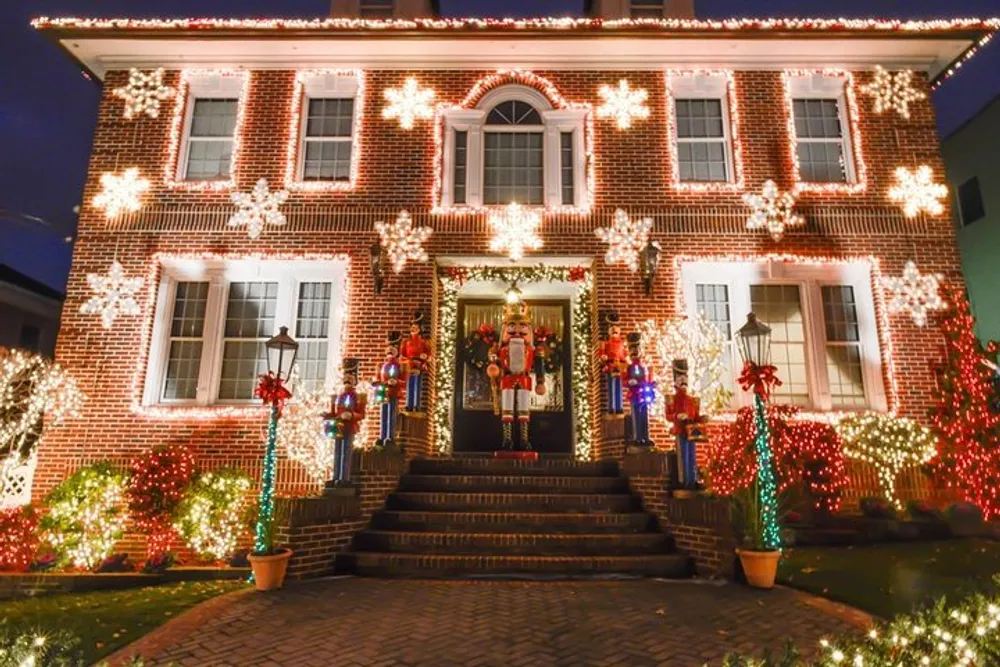 The image shows a two-story brick house festively decorated with an abundance of Christmas lights snowflake motifs and oversized toy soldiers flanking the front door exuding a warm holiday spirit in the evening